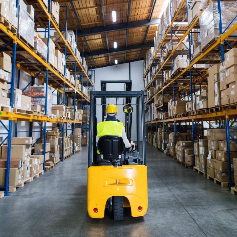 A forklift operator moving pallets down a warehouse aisle