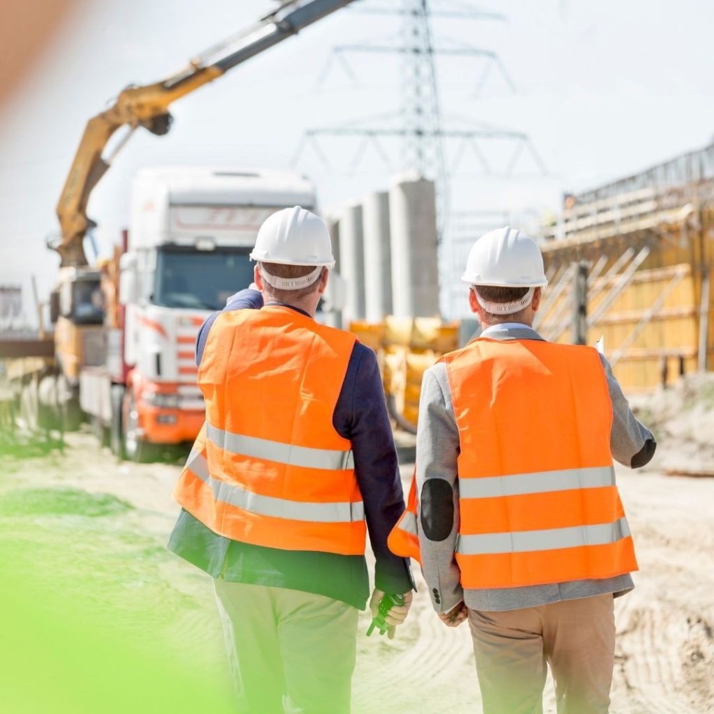 Two workers in hi-vis vests walking through a construction site past a truck and crane